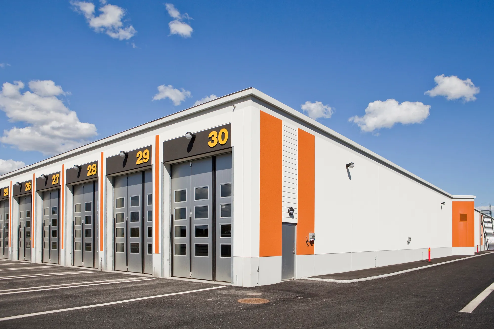Angled exterior view of a modern flex industrial facility featuring numbered garage bay doors and bright orange architectural accents under a blue sky in Houston, TX