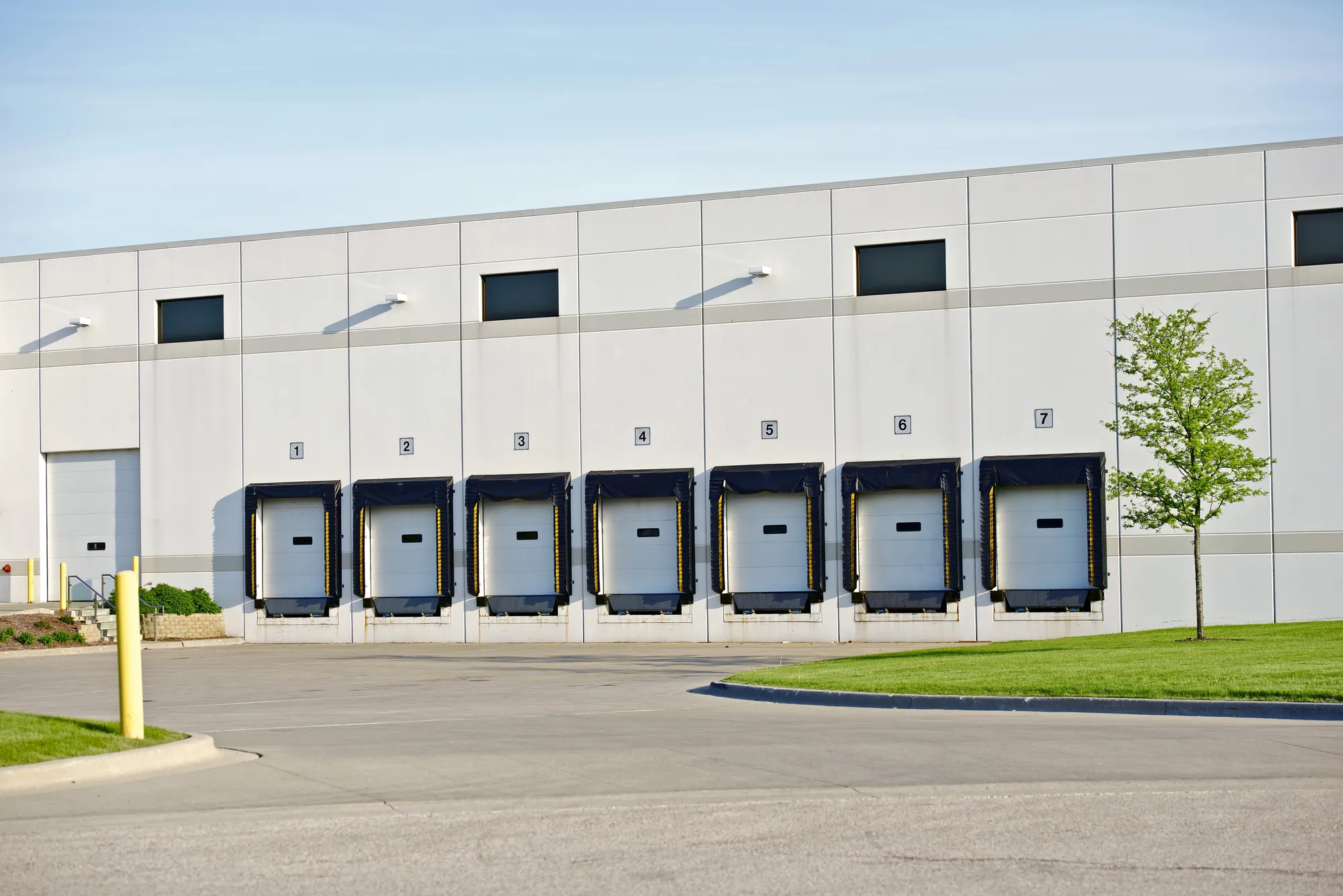 Exterior view of a modern Class A industrial warehouse featuring seven numbered loading dock bays with black cushions and overhead doors in Los Angeles, CA