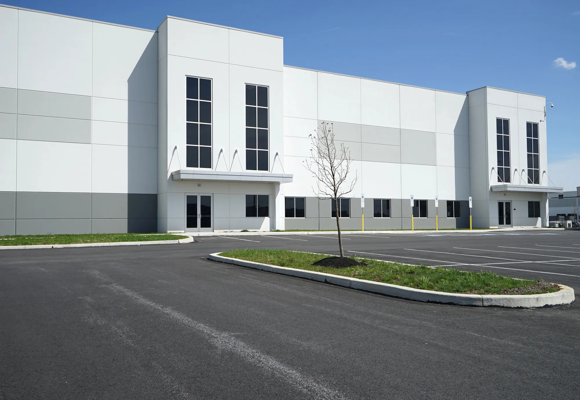 Angled exterior view of a modern white industrial warehouse corporate office facility featuring twin vertical glass windows and a landscaped parking lot island in Miami, FL
