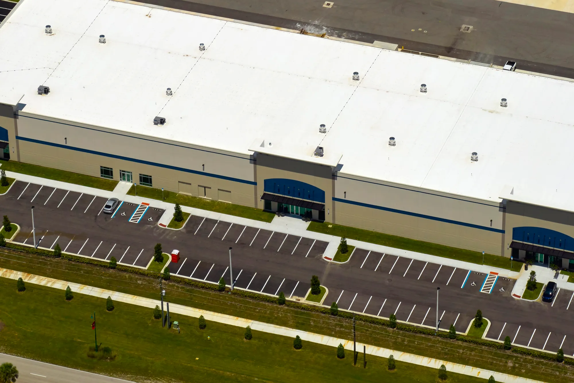 High-angle aerial view of a clean beige commercial warehouse building showing an expansive white roof and a newly striped asphalt parking lot in Ocala, FL