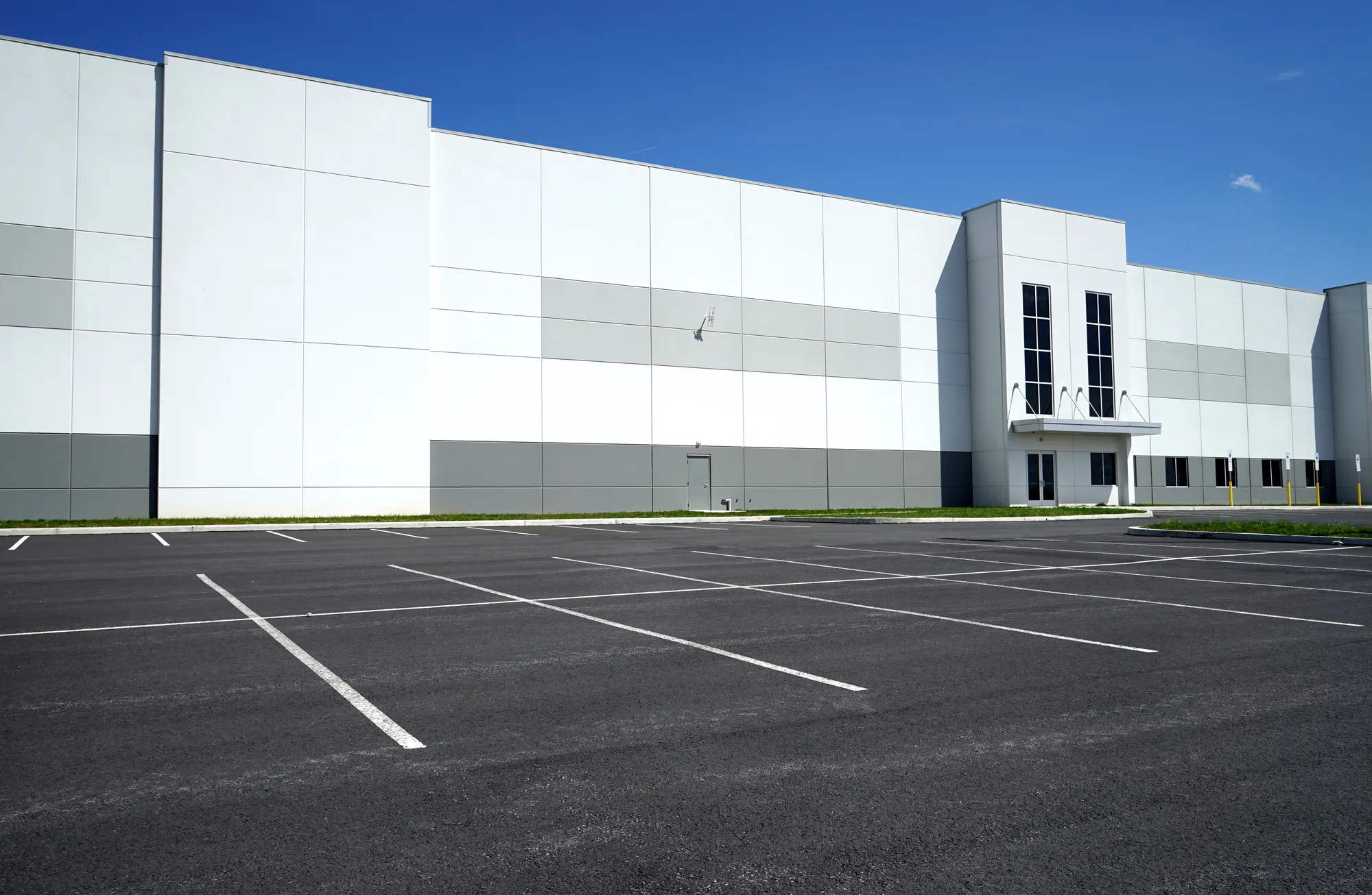 Exterior view of a massive Class A white e-commerce logistics warehouse building with a freshly paved empty asphalt parking lot in Phoenix, AZ