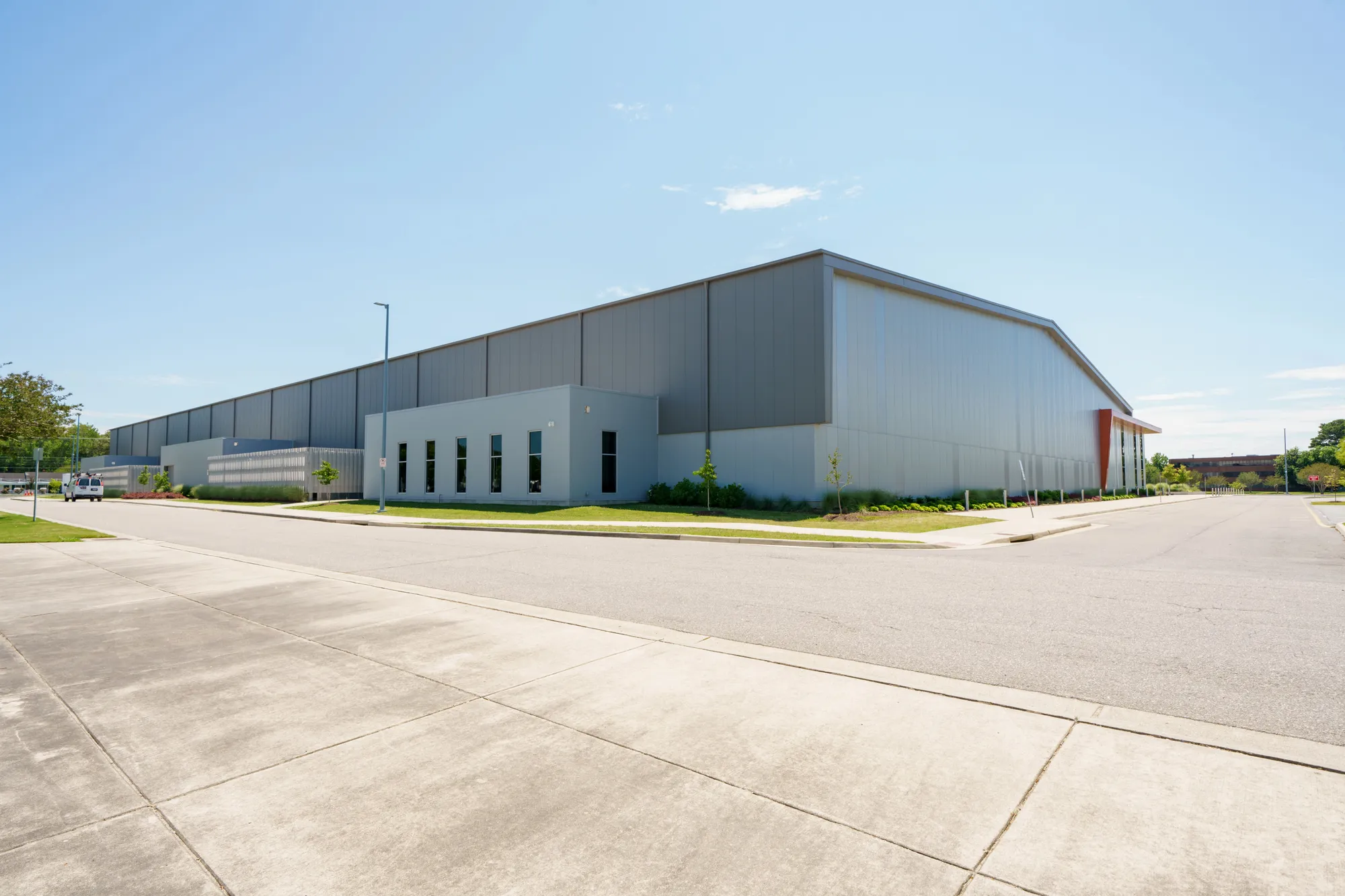 Angled exterior view of a modern, large-scale grey corrugated metal industrial warehouse facility with an attached single-story corporate office wing in Dallas, TX
