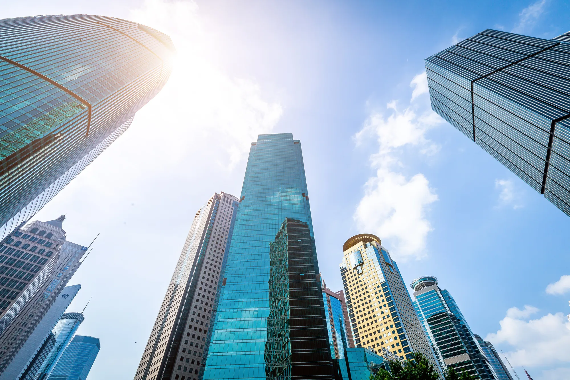 Low angle upward view of ultra-modern glass commercial skyscrapers in a downtown business district with bright sunlight flaring behind a high-rise tower in Austin, TX