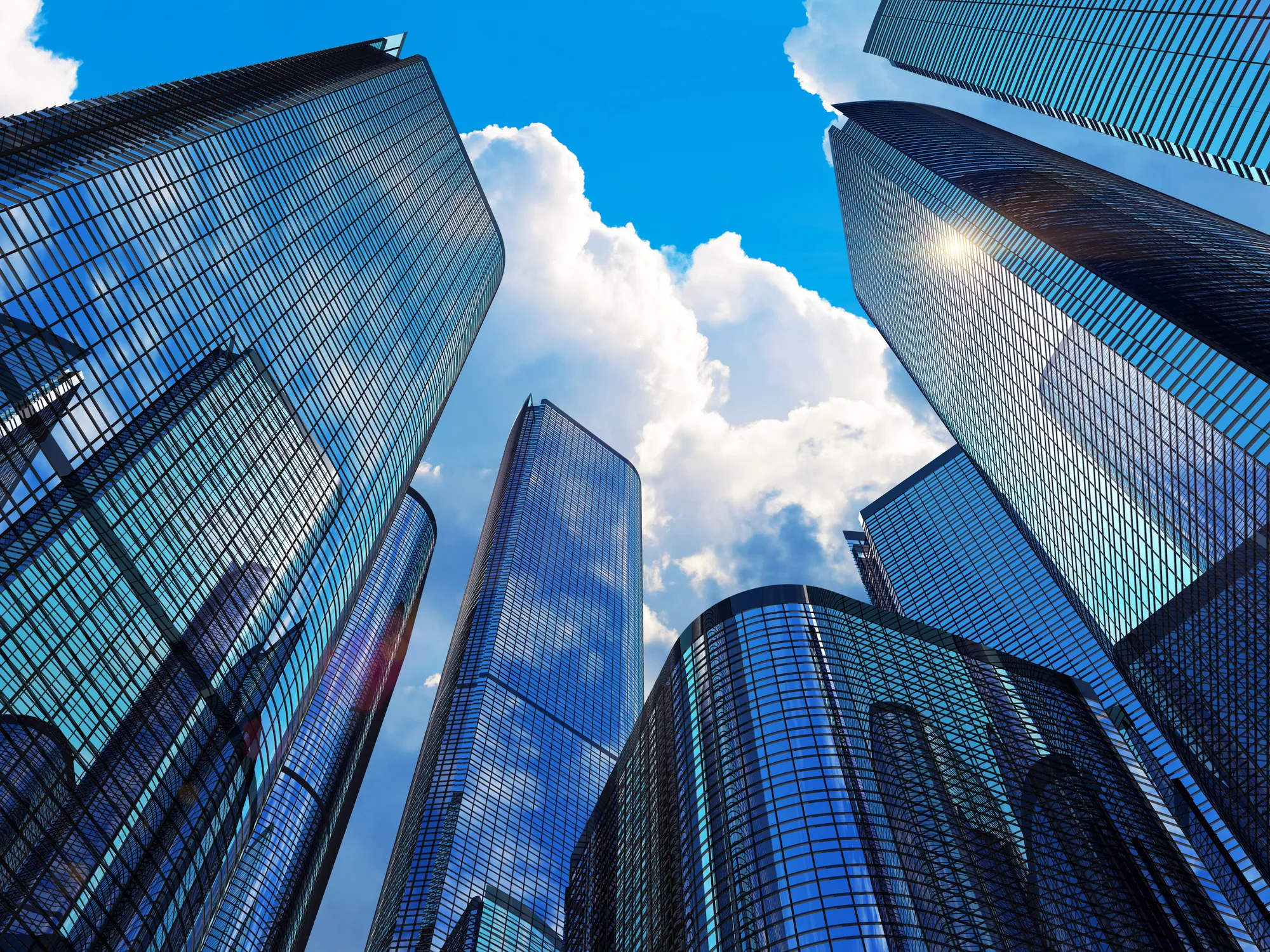 Low angle upward-looking view of towering modern glass and steel commercial skyscrapers reflecting bright clouds and sunlight in a downtown financial district in Miami, FL