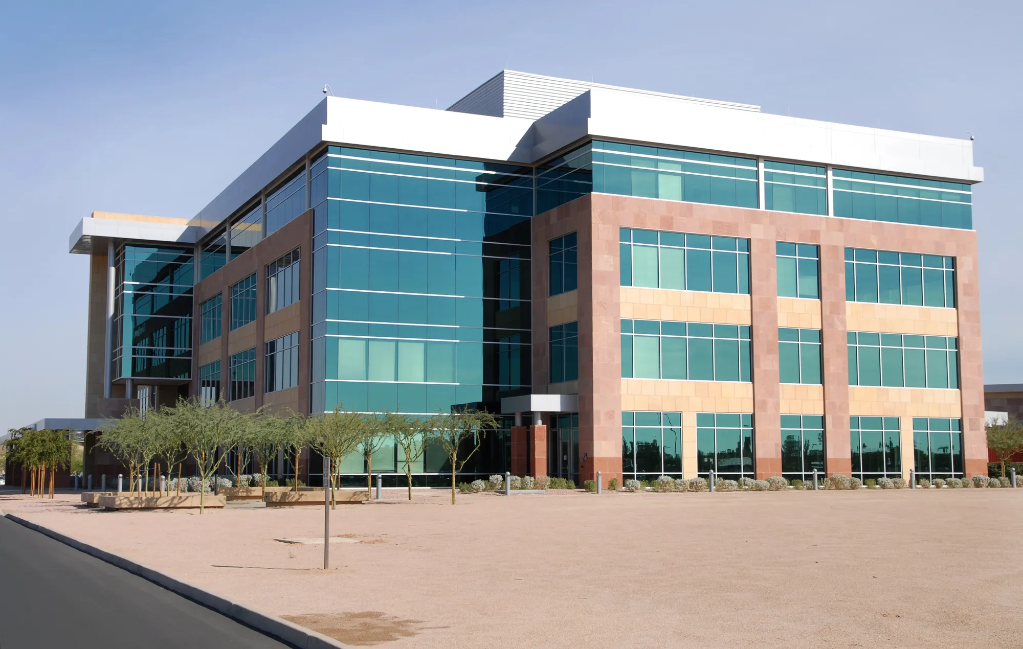 Exterior view of a modern four-story corporate office building featuring a green reflective glass curtain wall, stone panel accents, and a wide open plaza in Bennington, VT