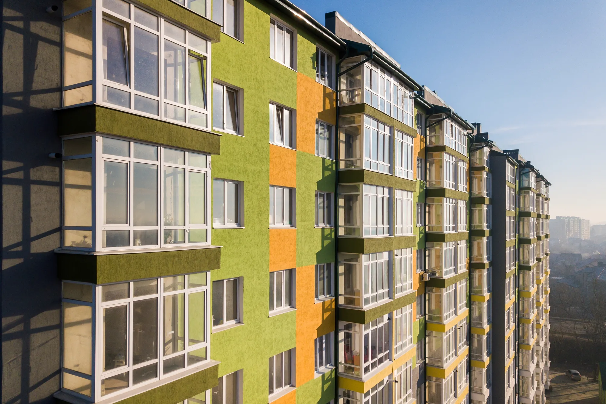 Angled high-angle view of a modern multi-story multifamily apartment building featuring a bright lime green, orange, and olive facade with glass balconies in Chicago, IL