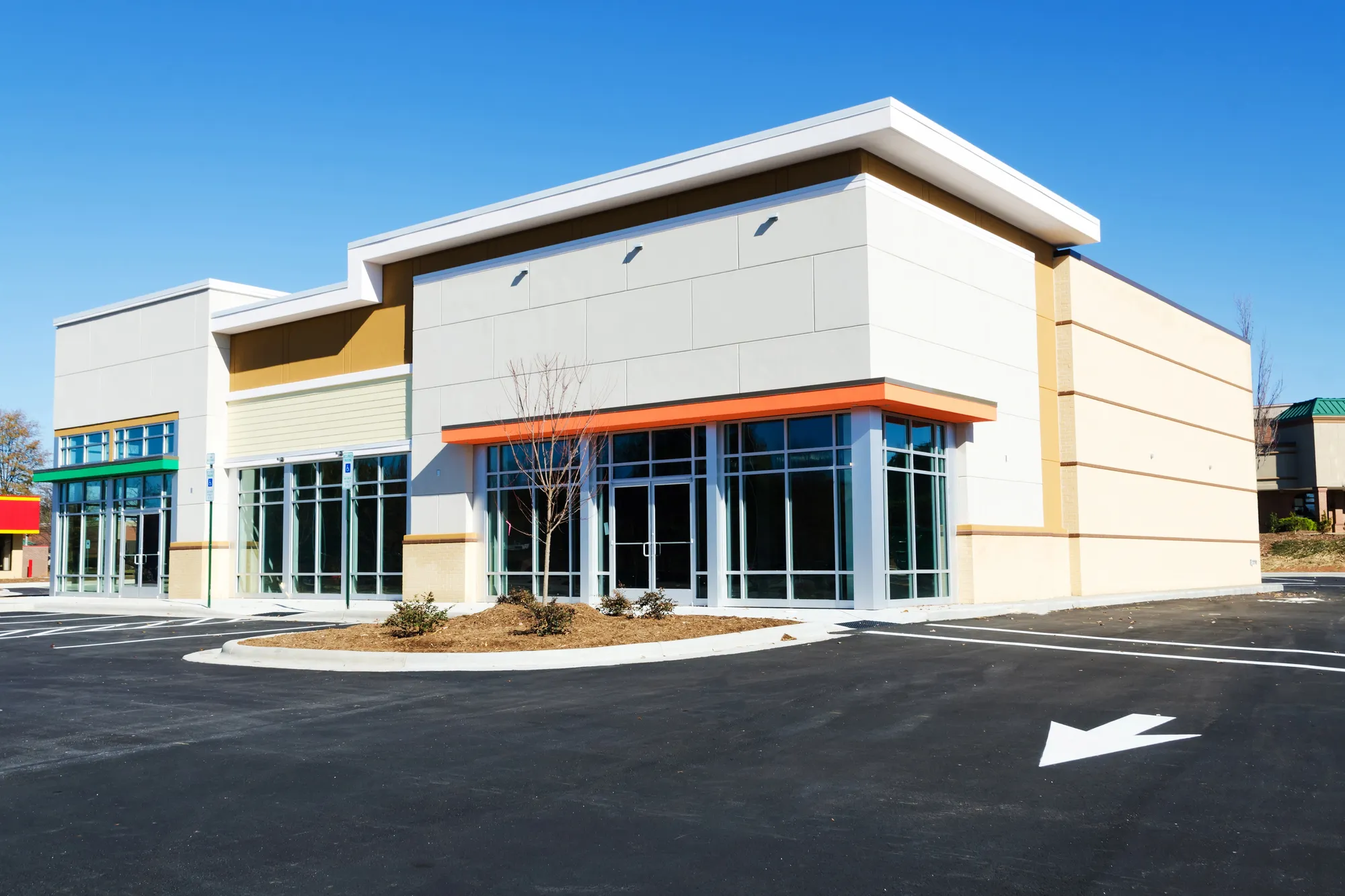 Angled exterior view of a newly constructed modern multi-tenant commercial retail strip center featuring large glass storefront doors and an empty asphalt parking lot in Elgin, IL