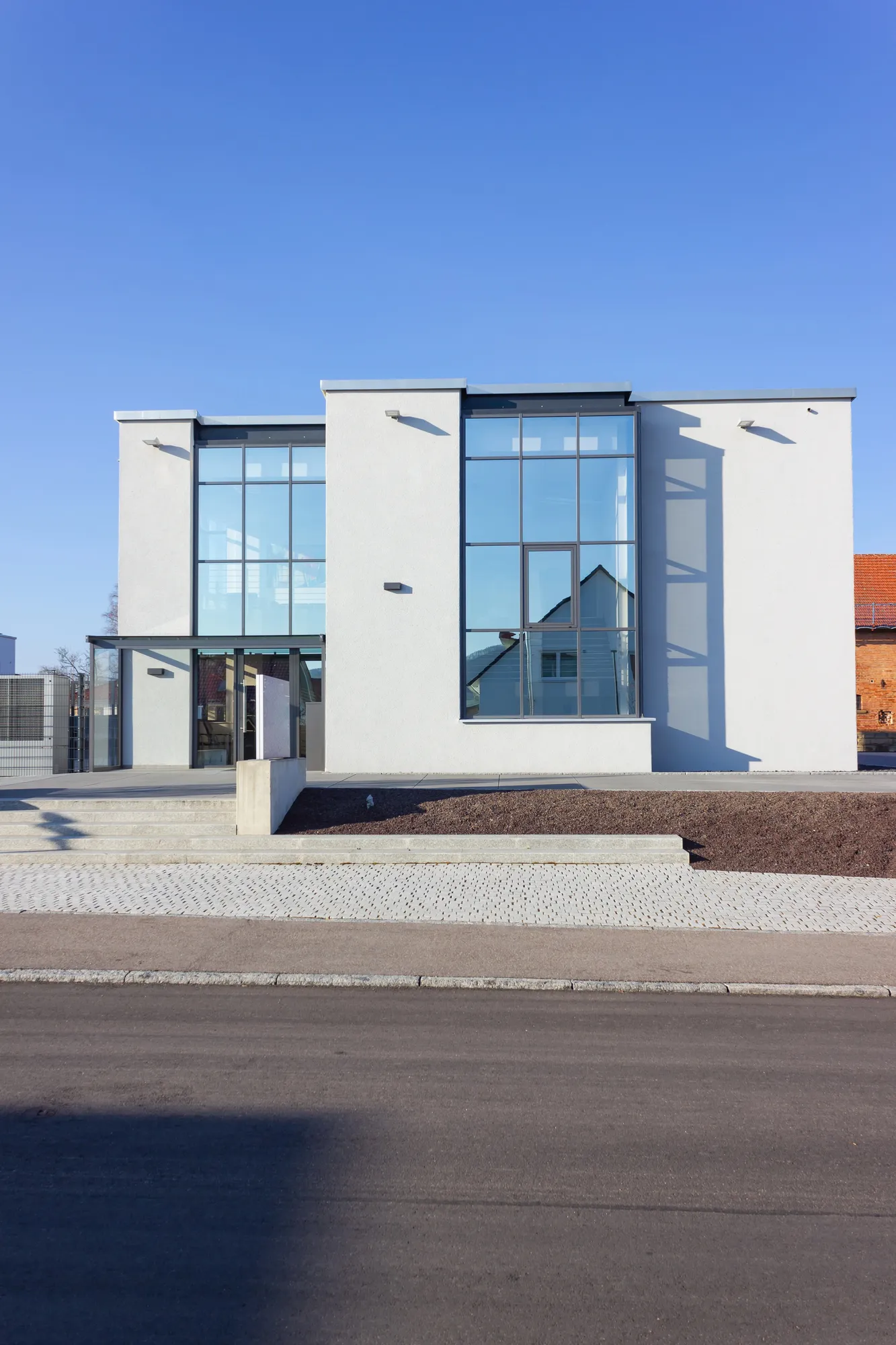 Front exterior view of a minimalist two-story white commercial office building featuring expansive multi-pane glass facade windows under a clear blue sky in Durham, NC