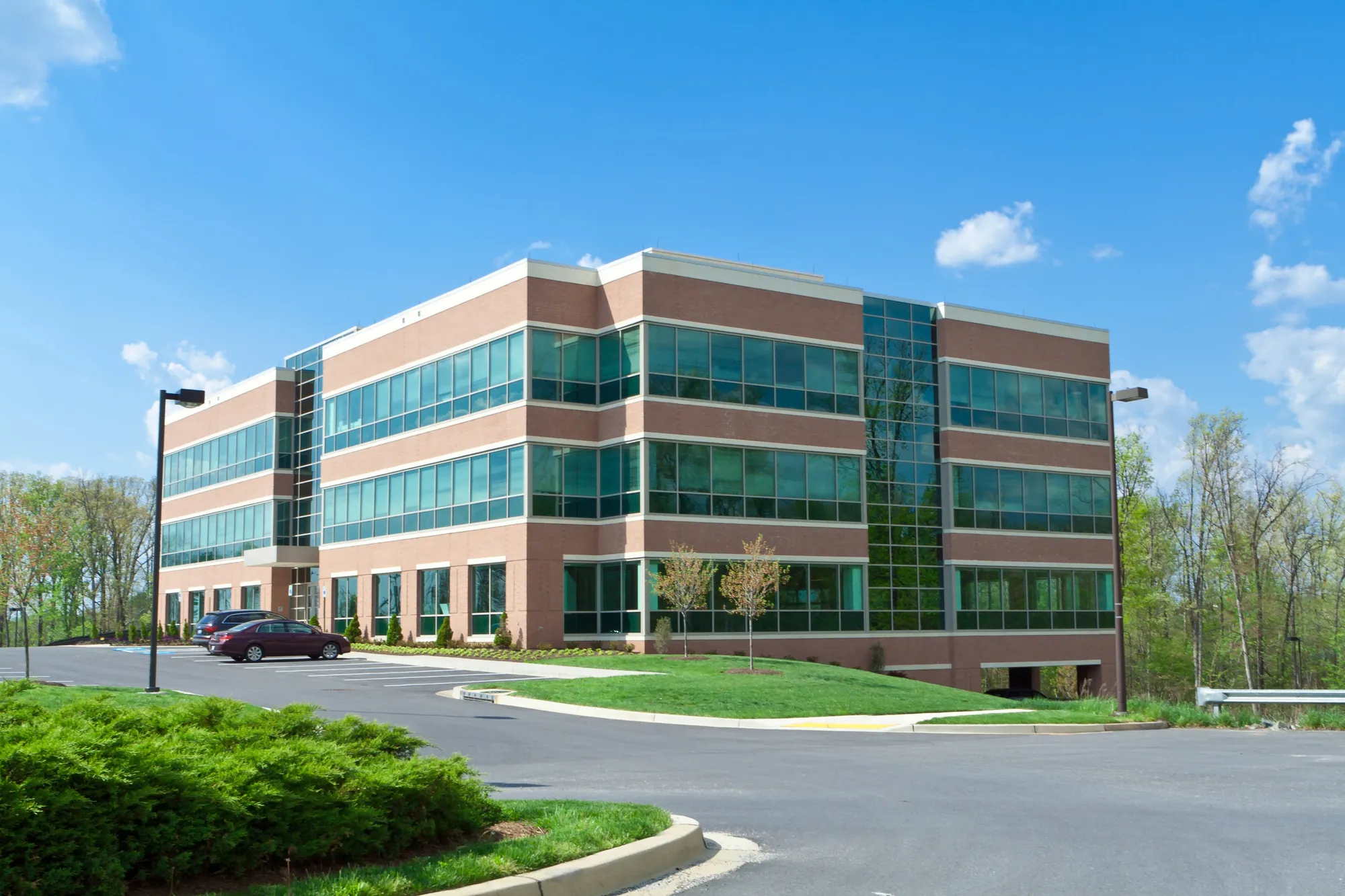 Exterior view of a modern three-story commercial brick and glass corporate office building featuring a clean asphalt parking lot and landscaped green grass lawn in Aurora, IL