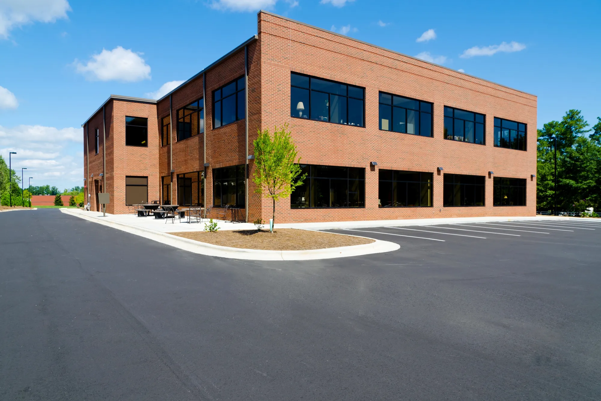 Angled exterior view of a two-story red brick commercial corporate facility with an empty asphalt parking lot and outdoor patio seating in Naperville, IL